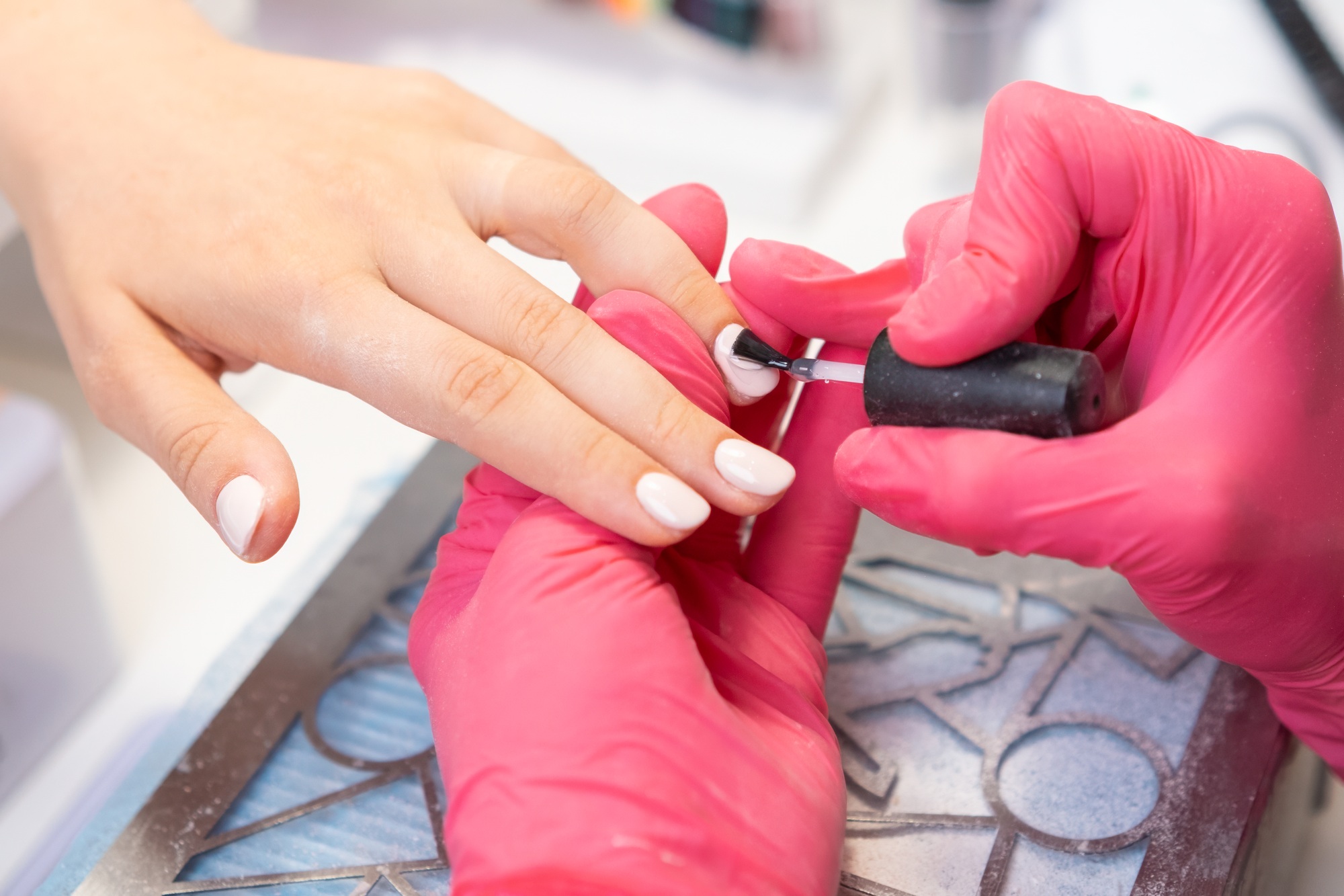 Client receives a top layer of gel polish application on her nails while relaxing in a nail salon.